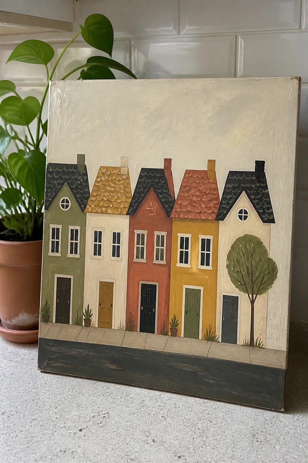 Colorful row houses painting on canvas beside leafy potted plant on countertop