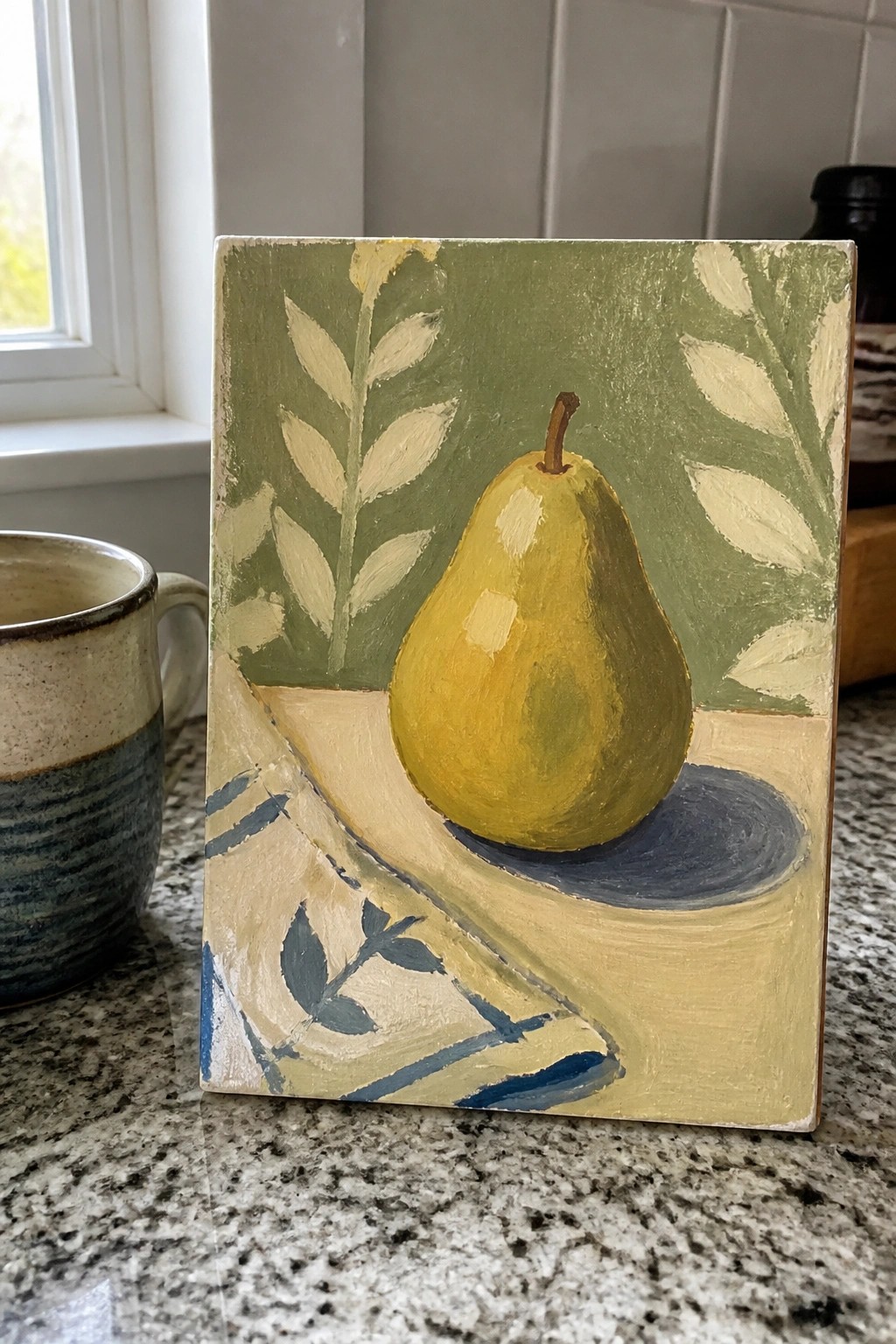 Yellow pear still-life painting beside ceramic mug on granite kitchen counter