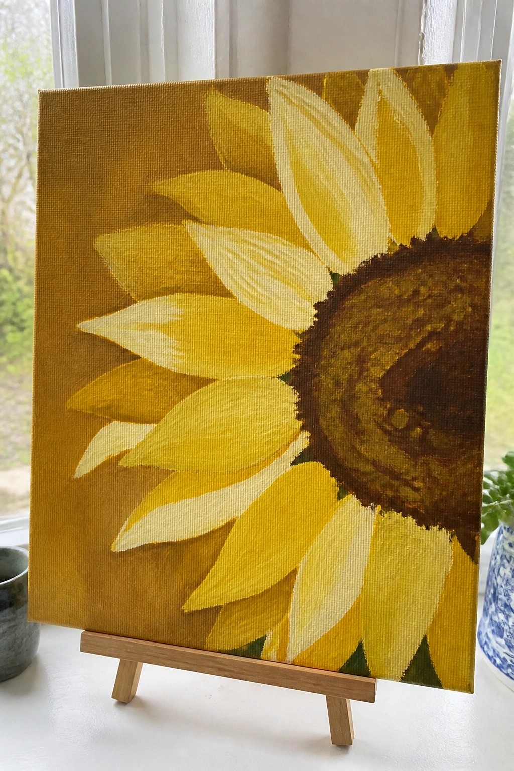 Yellow sunflower painting with brown center on canvas atop wooden easel.