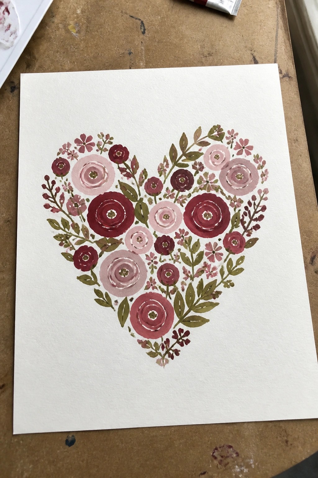 Watercolor heart formed from red and pink flowers with green leaves on paper