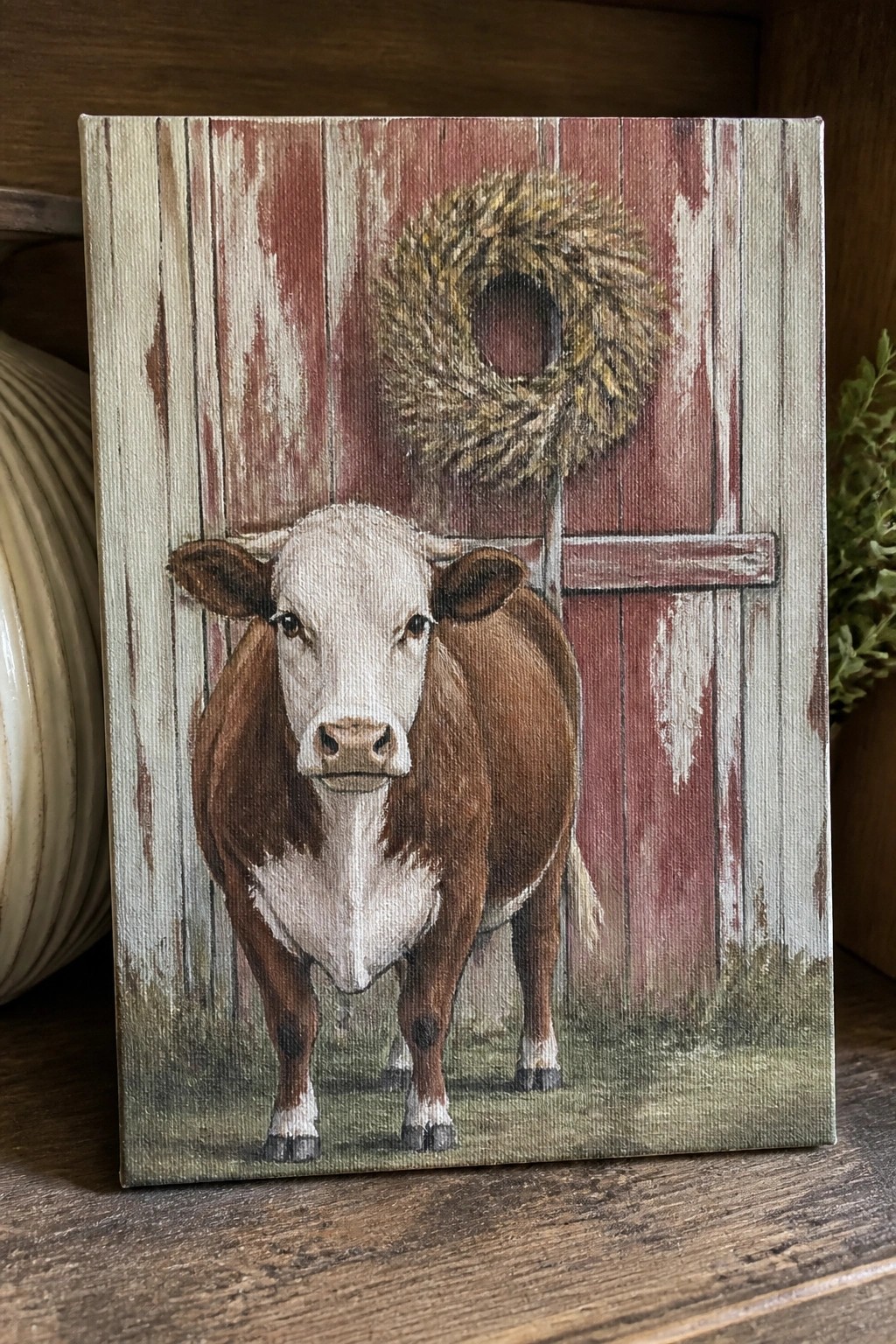 Brown and white cow stands before red barn door with hay wreath.