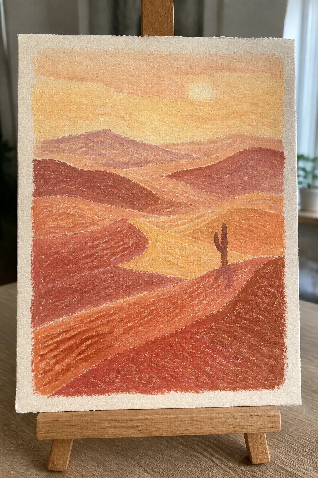 Colorful painting of sunset over red desert hills with a cactus on an easel.
