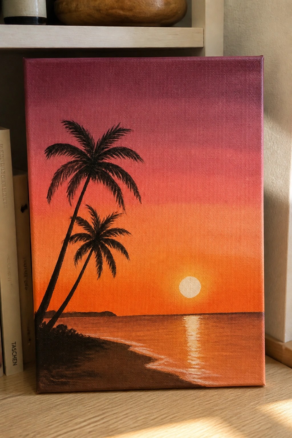 A canvas painting shows two black palm trees on the left silhouetted against a purple-to-orange gradient sky with a white sun and its reflection on the water below.