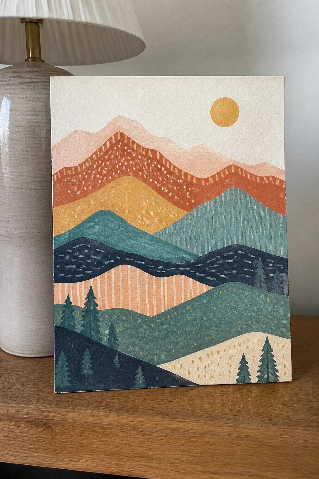 Abstract mountain painting with layered orange teal peaks, golden sun, trees beside lamp.