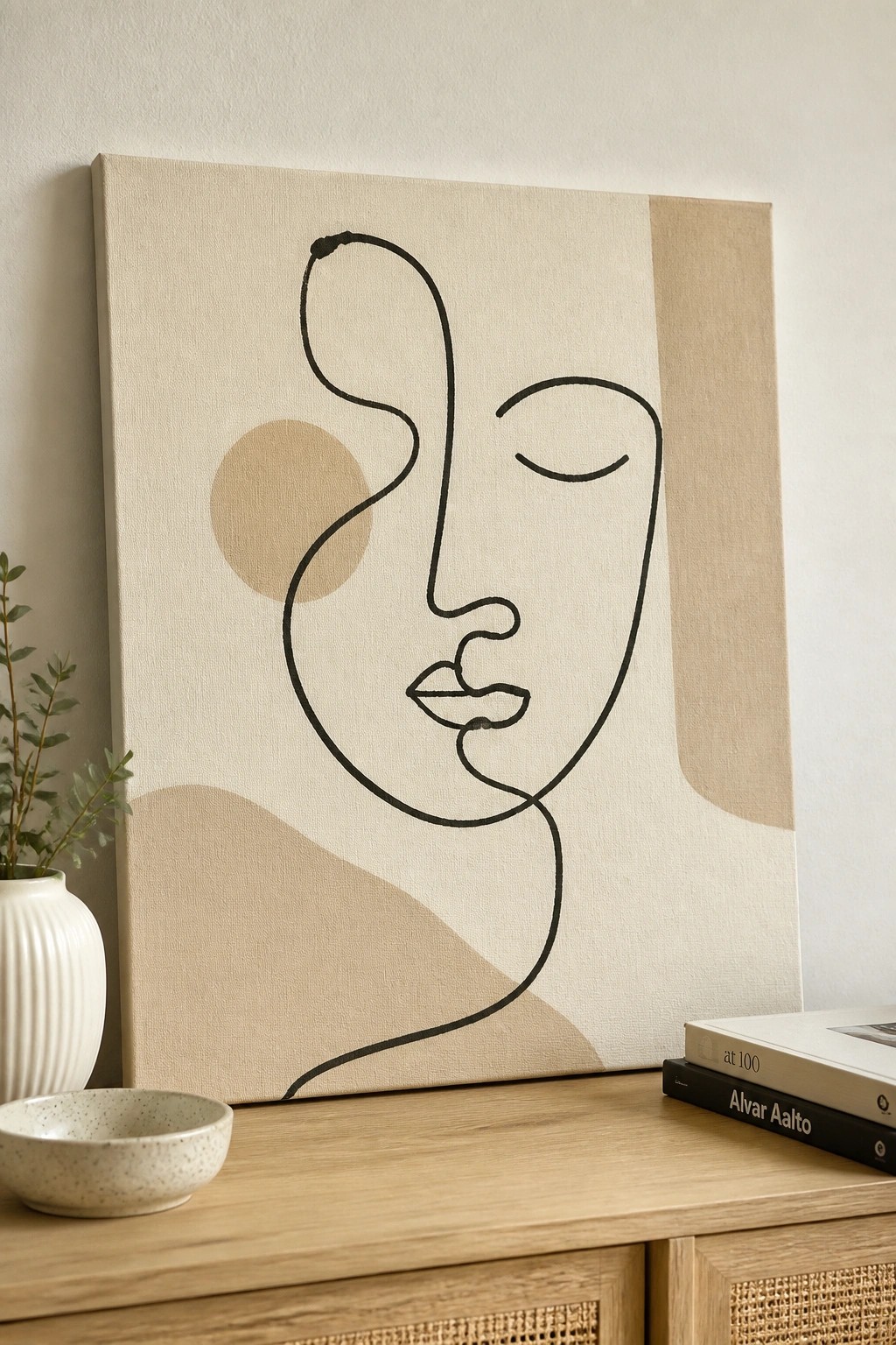 Abstract line art face on beige canvas beside books and bowl on wooden cabinet