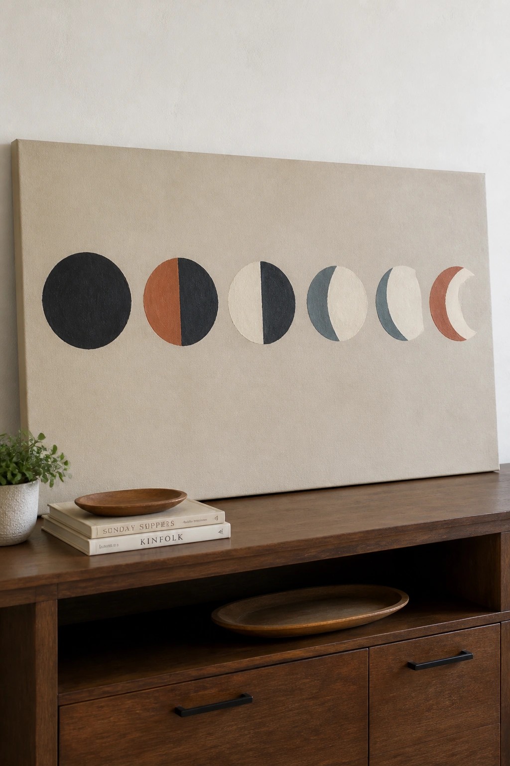 Minimalist moon phase artwork above wooden console with books, plant, and bowls