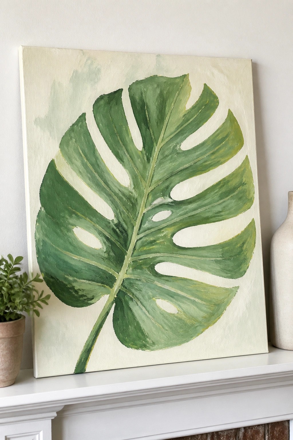 Large green monstera leaf painting on canvas atop white mantel with plant and vase