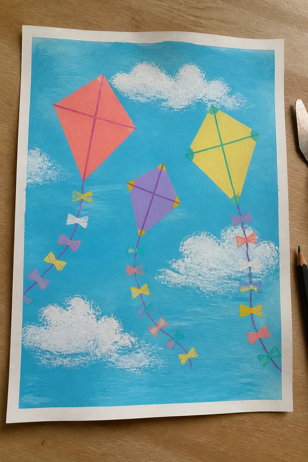 Three diamond kites in red, yellow, and purple with bow tails in blue sky.