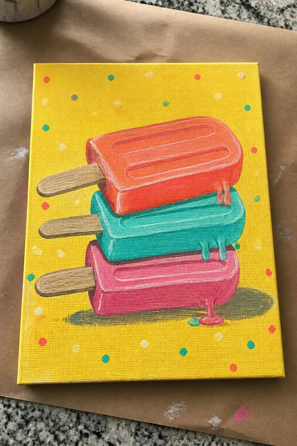 Three melting popsicles stacked on yellow polka-dotted canvas with colorful dots.