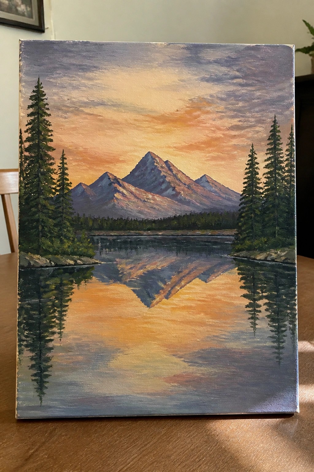 Landscape painting of mountains reflected in a lake at sunset with pine trees.