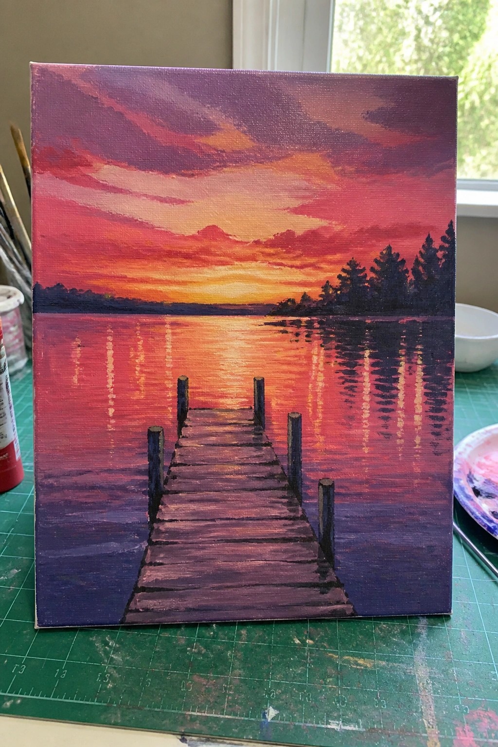 Vibrant sunset painting with red-orange sky, reflective lake, and wooden dock.