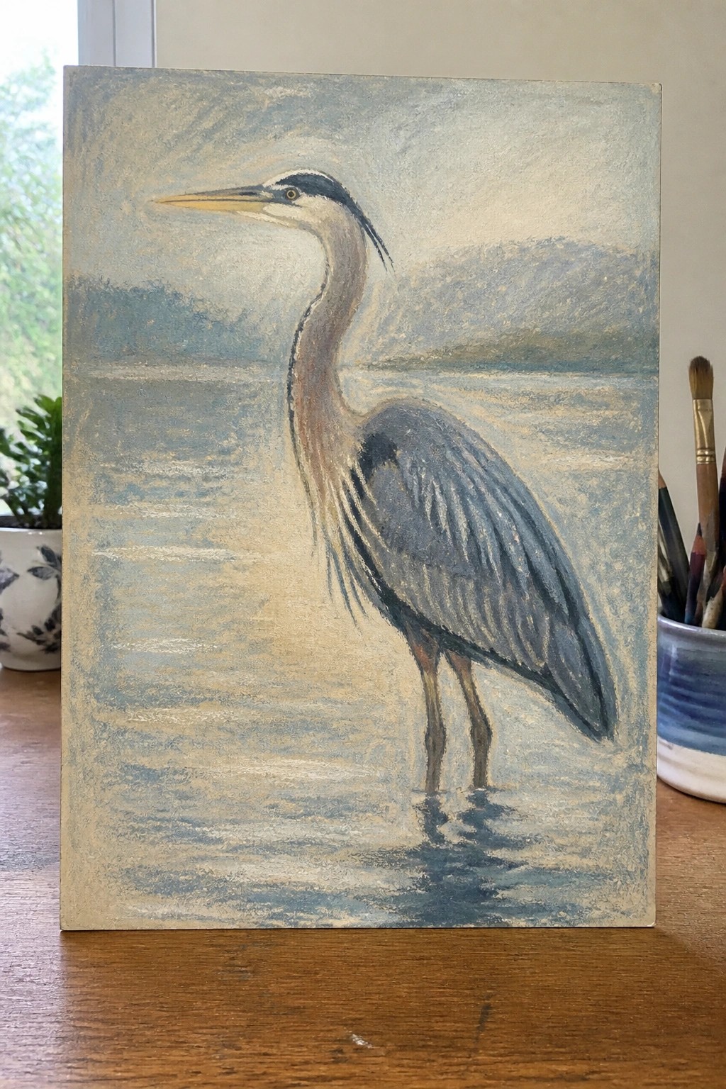 A painting of a great blue heron standing in shallow water with soft blue and gray background tones.