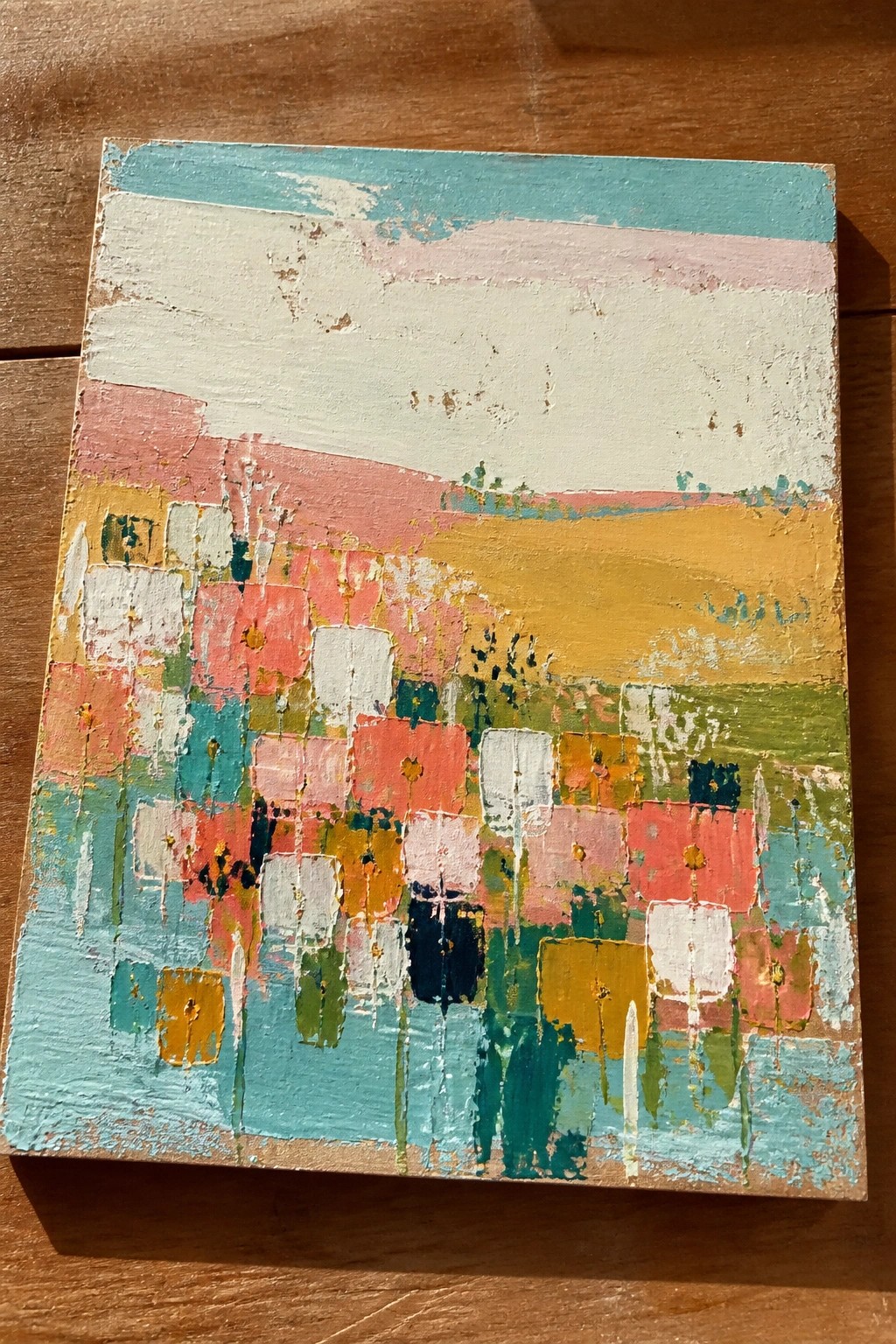 Abstract painting with colorful pink, blue, yellow, and green blocks on wood.