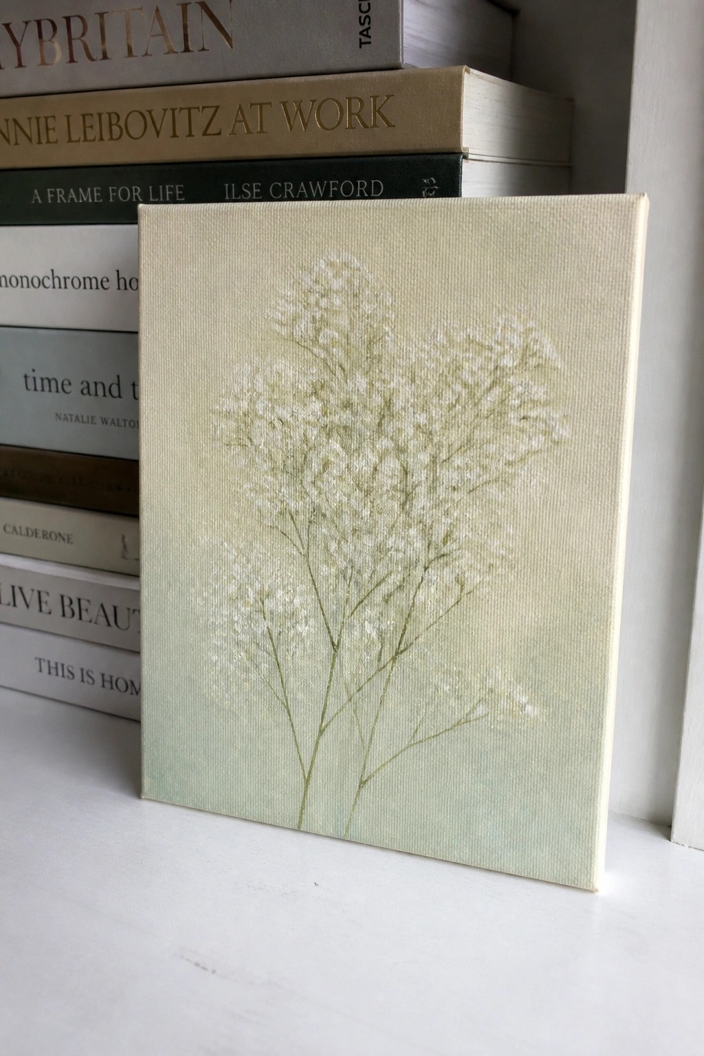 Canvas with delicate white flowers leaning against stacked books