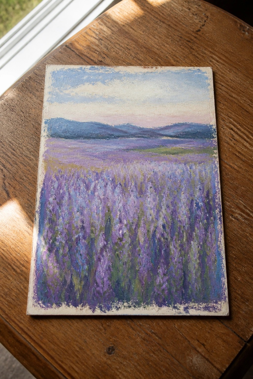 Pastel painting of purple lavender field with blue mountains on wooden table