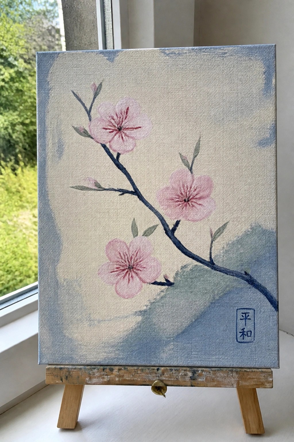 Pink cherry blossoms on branch painted on canvas atop wooden easel.