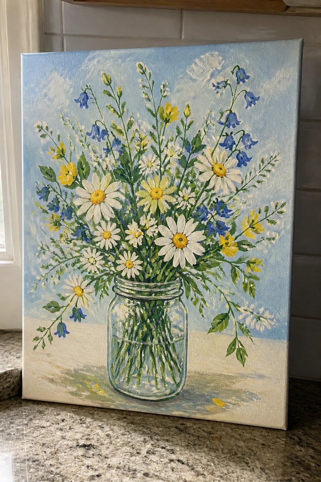 Vibrant wildflower bouquet of daisies and bluebells in glass mason jar on canvas.