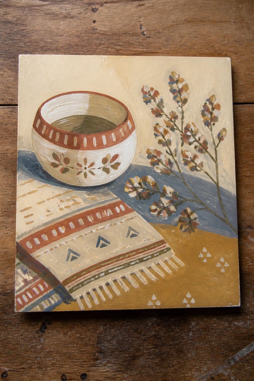 Decorated ceramic bowl beside patterned fringed textile and colorful dried flowers.