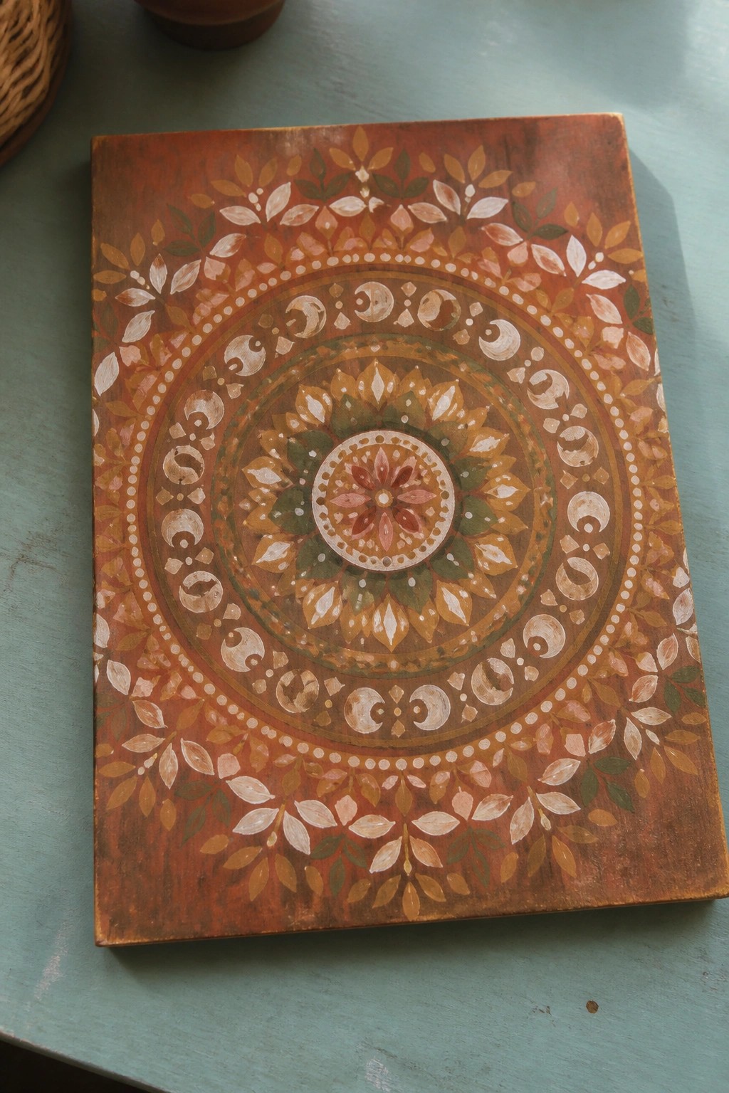 Mandala artwork with floral crescents and leaves in earthy tones on wood