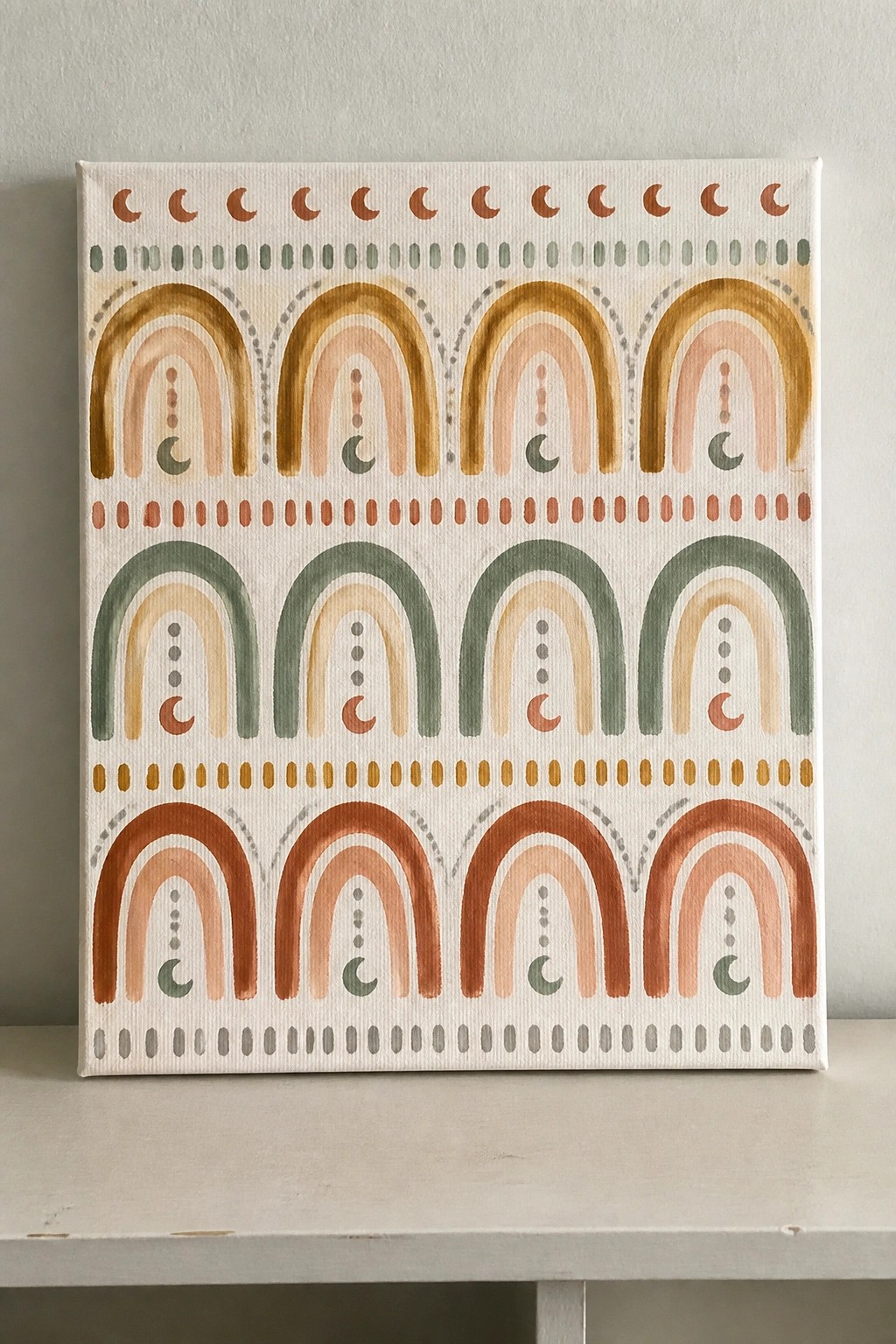 Boho canvas painting with layered rainbow arches, crescent moons, and dotted borders in earthy tones.