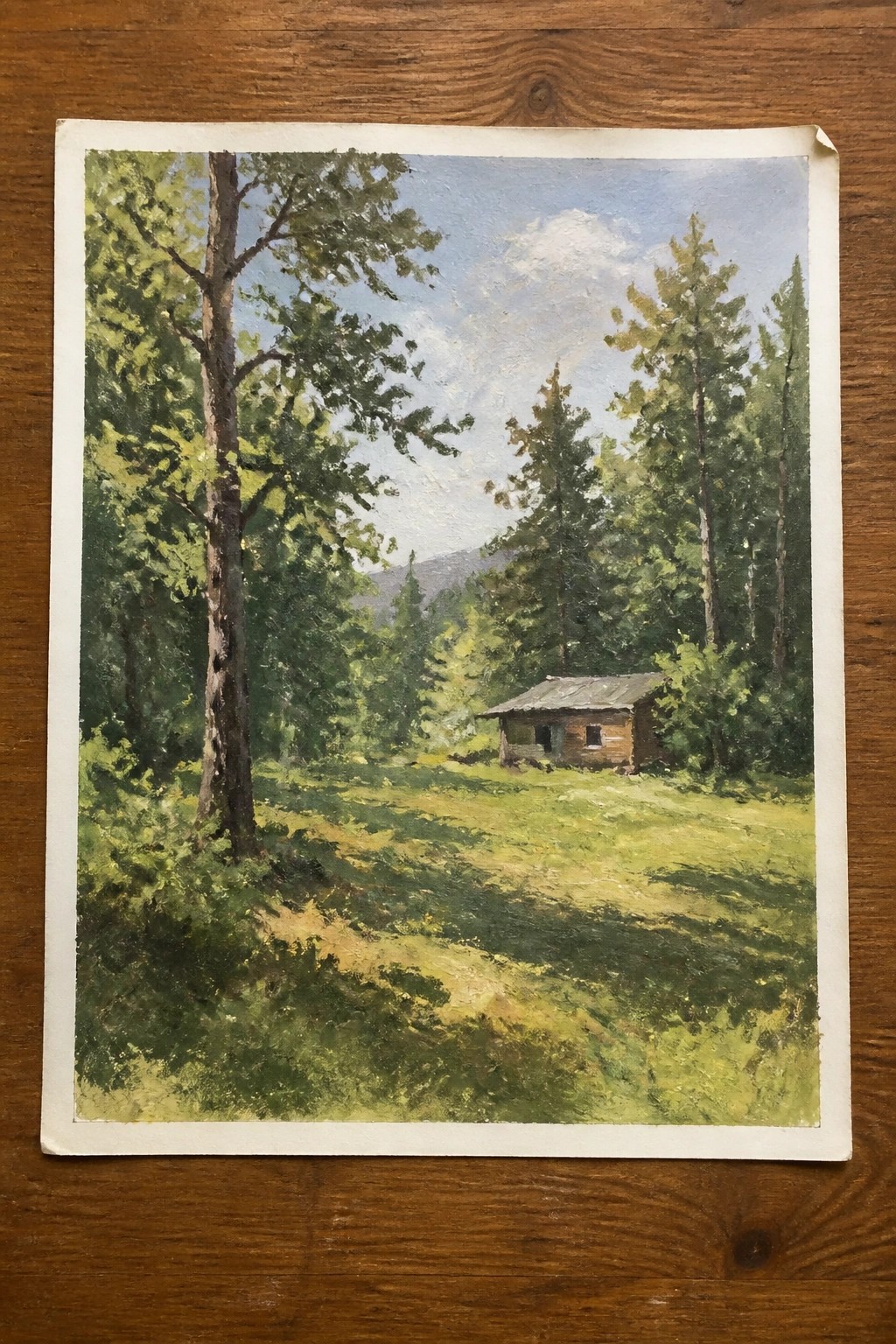 Landscape painting of rustic cabin in sunlit forest clearing with tall trees and mountains.