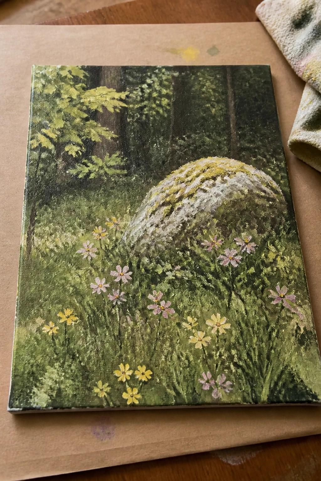 Mossy boulder amid yellow and pink wildflowers in lush forest painting