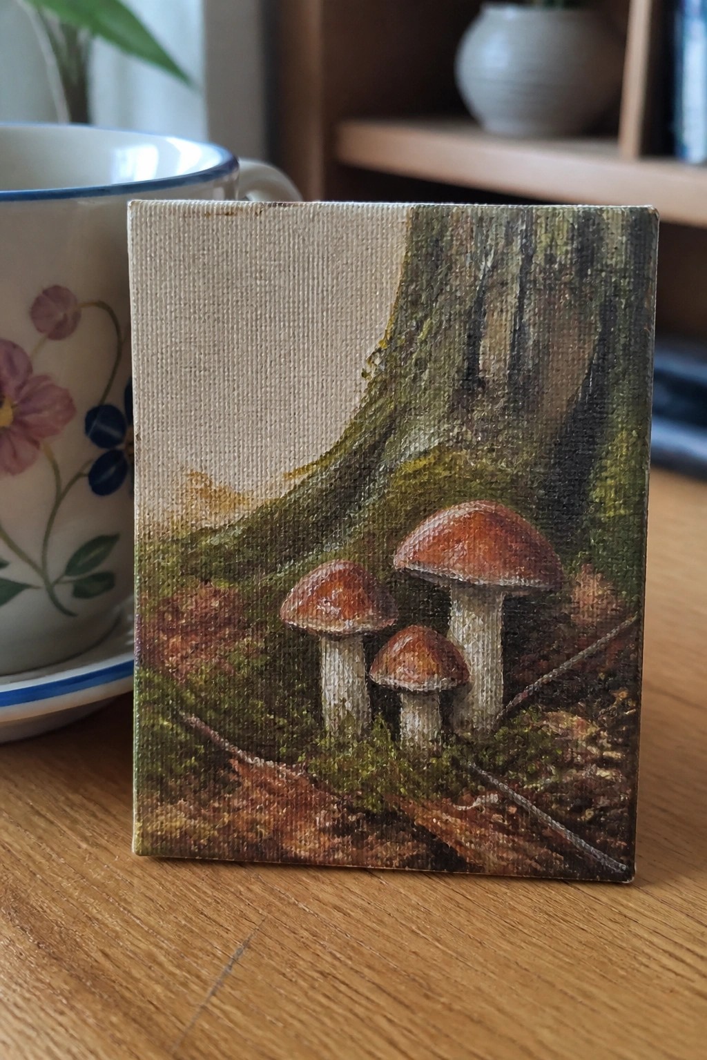 Small canvas painting of three brown mushrooms at a tree base