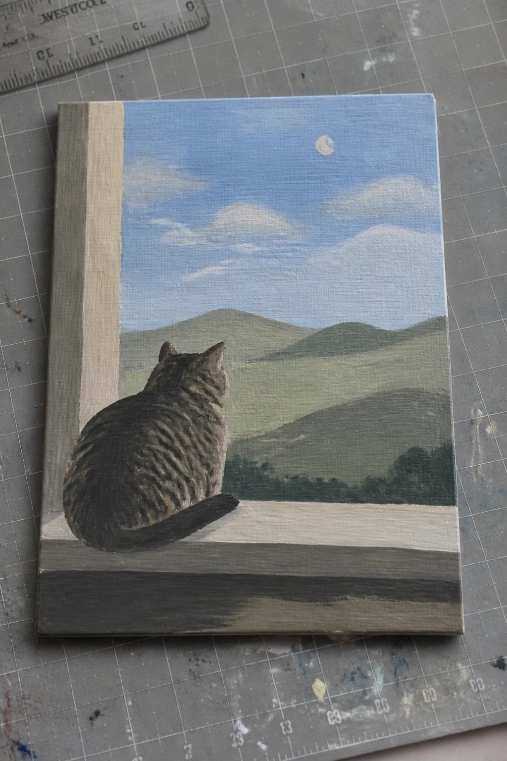 Tabby cat on ledge views green hills under blue sky with clouds and moon