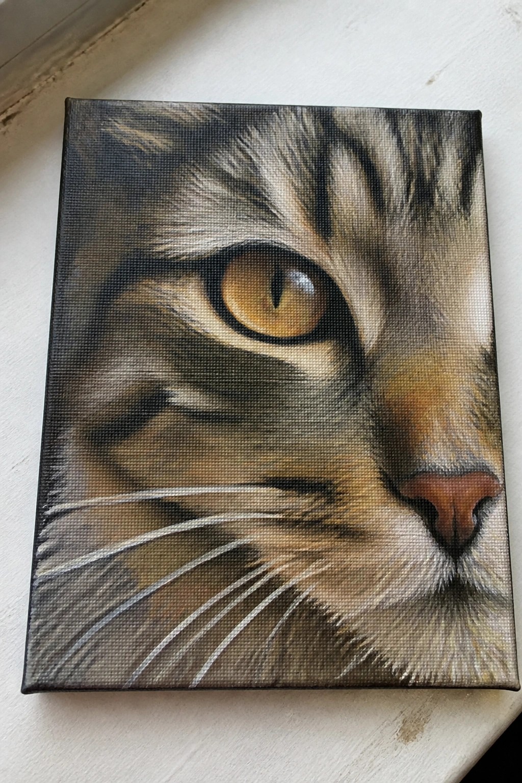 Realistic canvas painting of tabby cat face with amber eye, whiskers, and pink nose