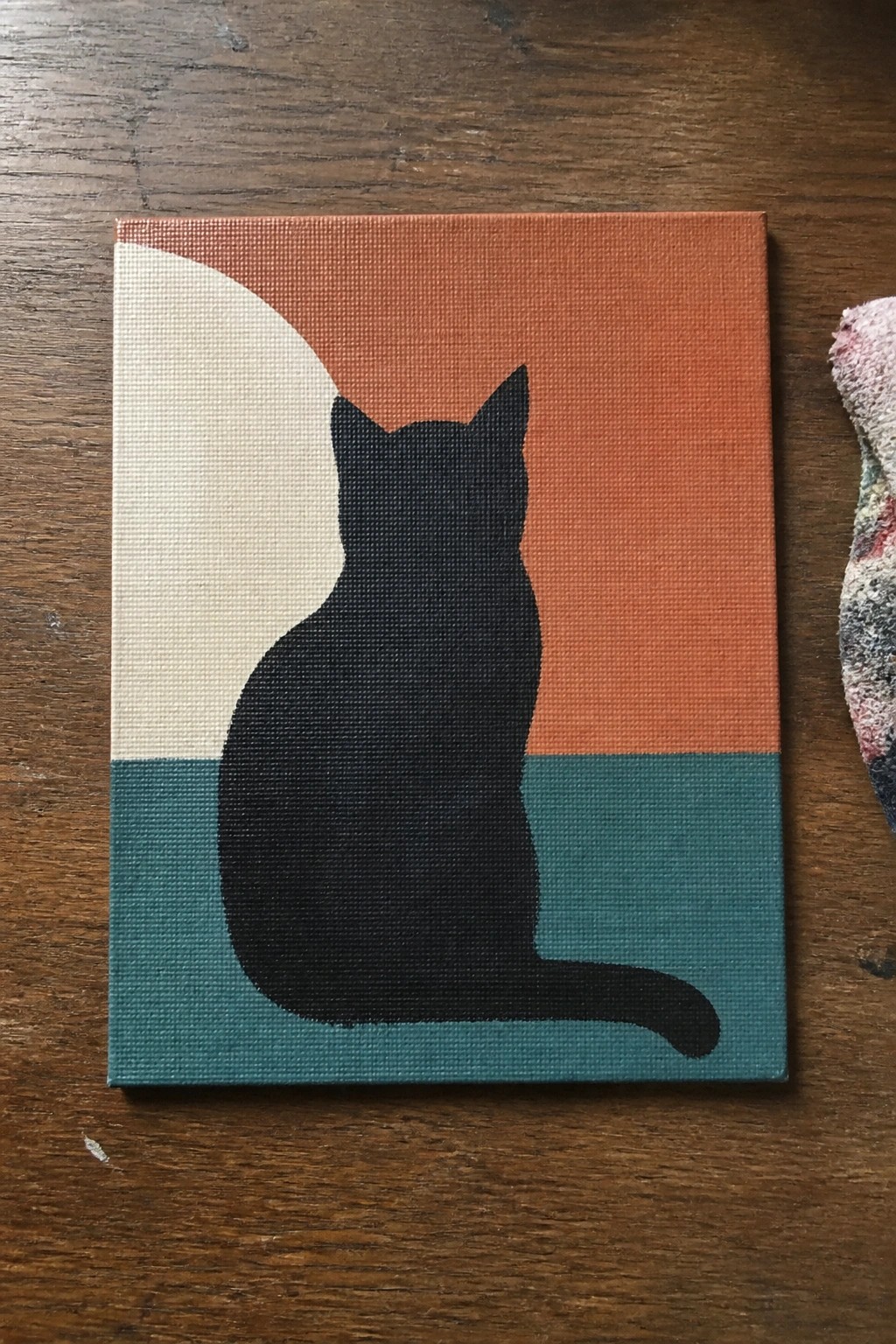 Black cat silhouette on canvas with orange, teal, and beige geometric shapes.