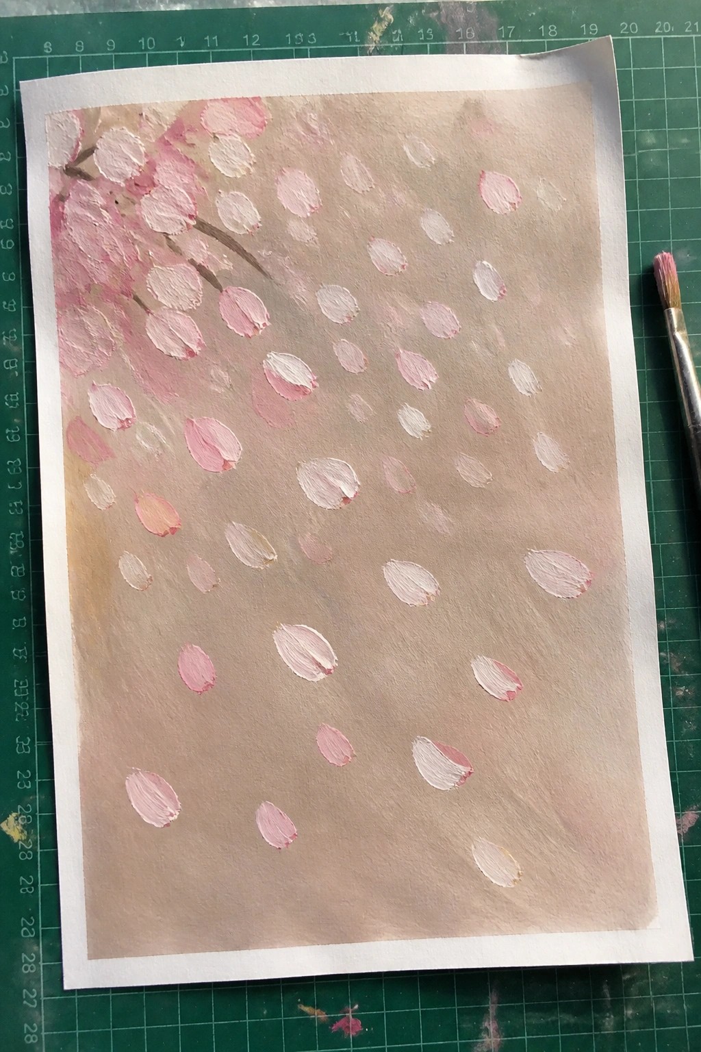 Painting of pink cherry blossom petals scattered on brown paper beside paintbrush on green mat