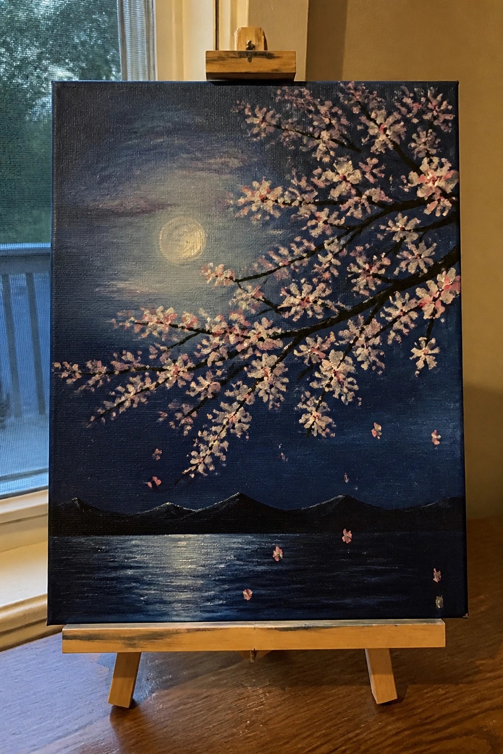 Night painting of cherry blossoms under full moon above dark water on easel