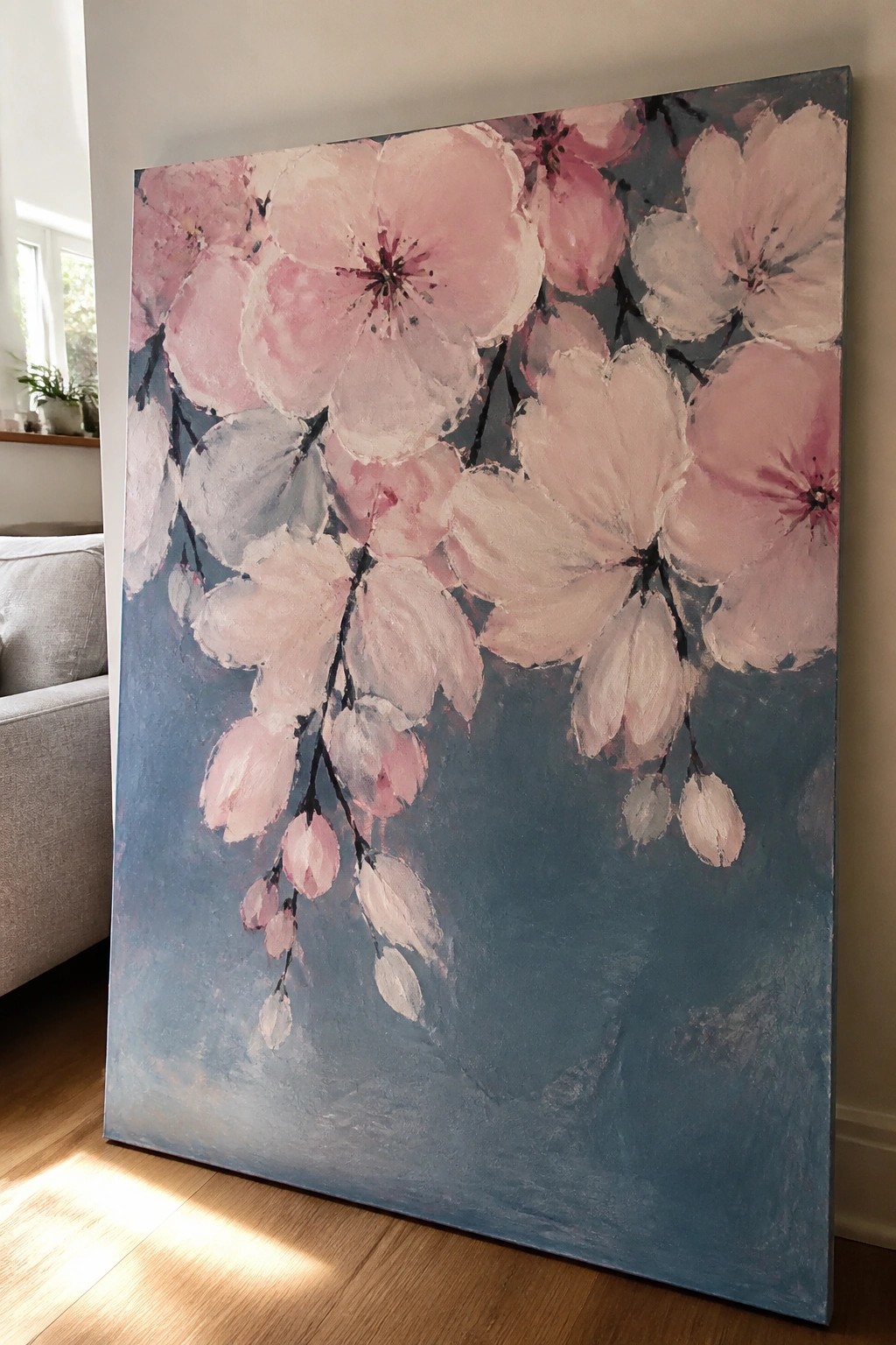 Large impressionistic painting of pink cherry blossoms on blue background leaning on wall.