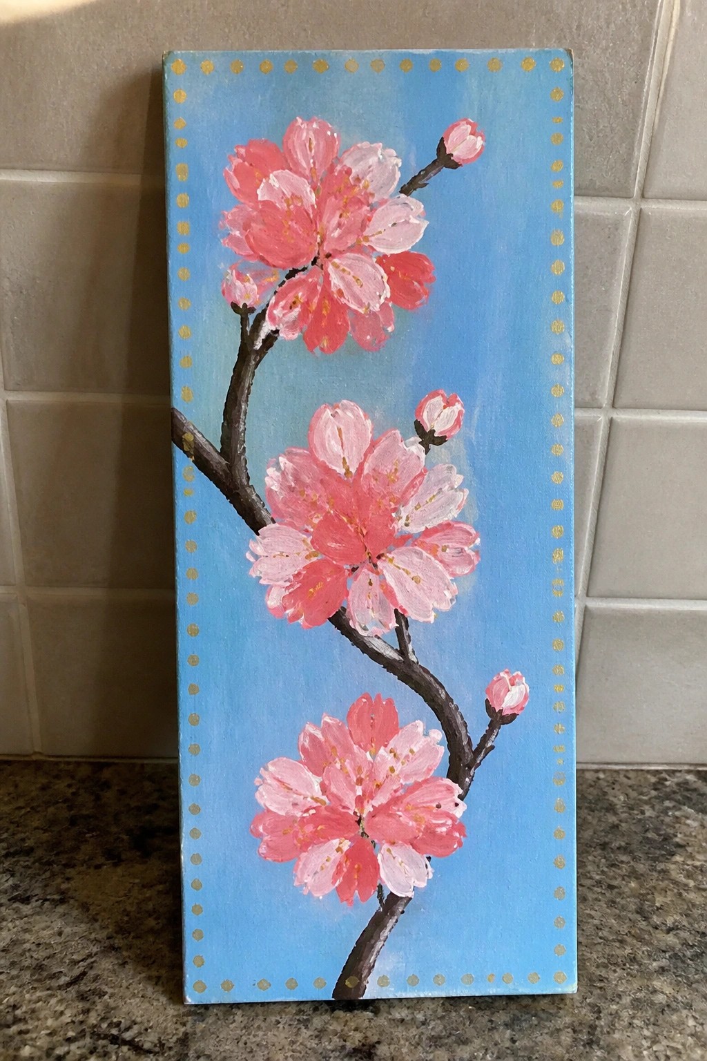 Pink cherry blossoms on branches against blue background with gold dotted borders.
