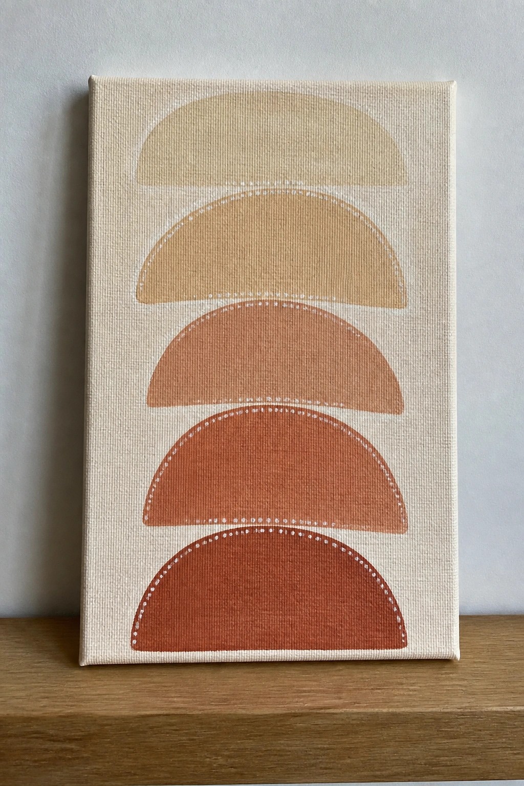 Canvas with five stacked semi-circles in warm neutral shades from beige to dark terracotta on an off-white background, each with a dotted white border.