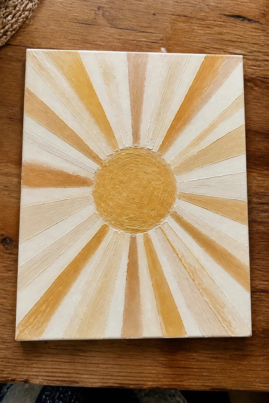 Sunburst painting with golden rays radiating from center on white canvas.