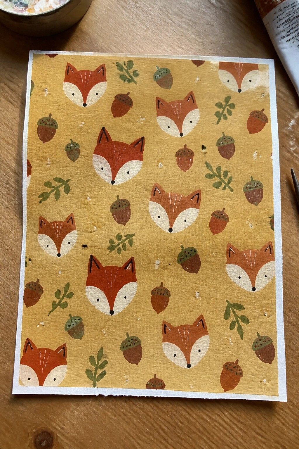 Stylized fox faces, acorns, and leaves patterned on mustard yellow paper.