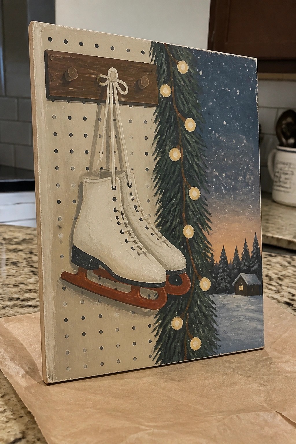 White ice skates hanging from wooden pegs beside lit Christmas tree and snowy cabin scene