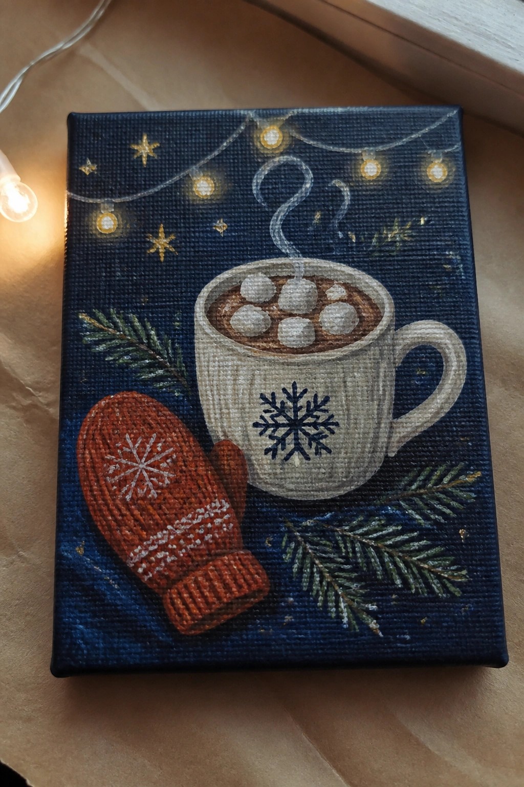 Cozy winter painting of red mitten, snowflake mug of hot cocoa, lights and pine on blue