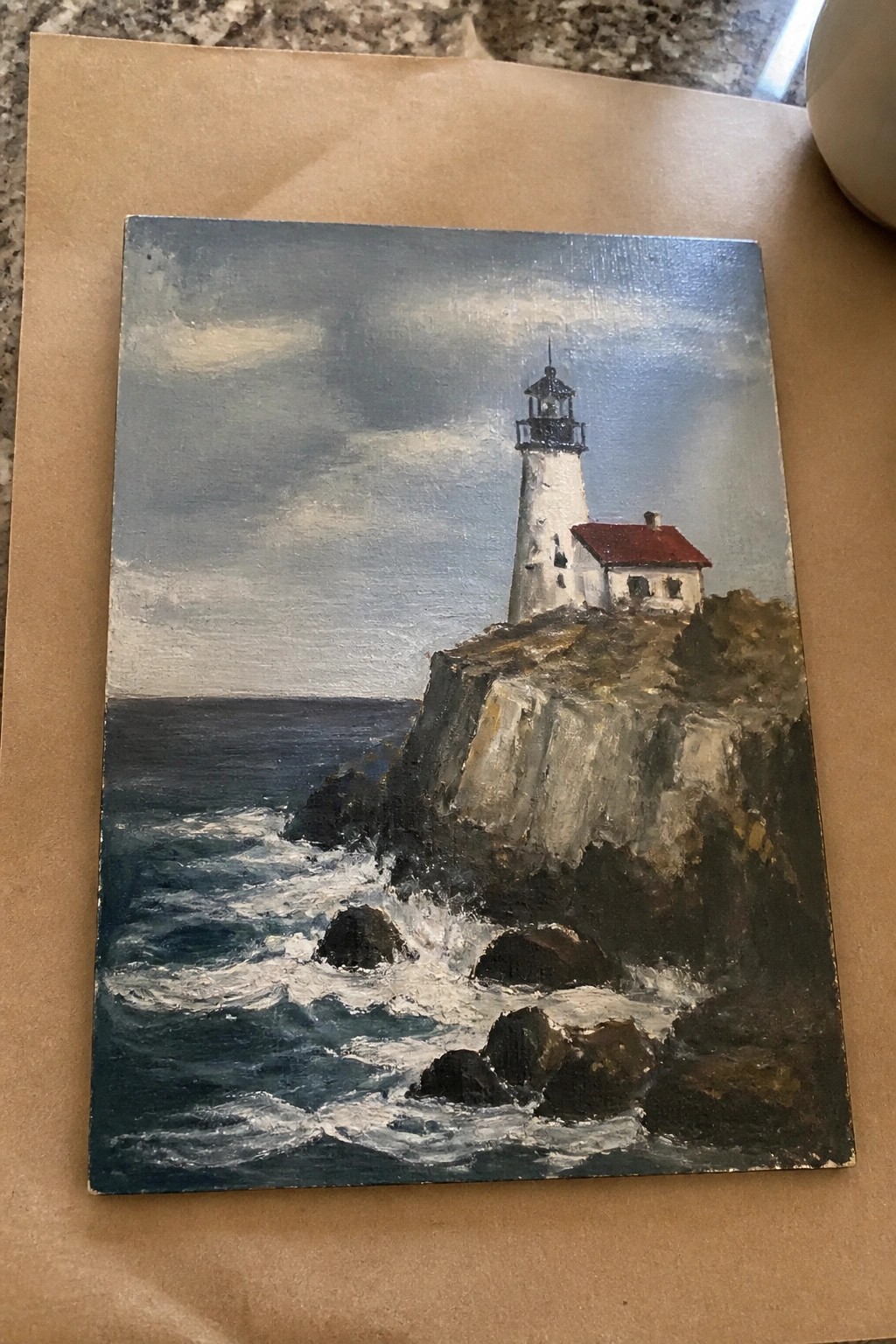 White lighthouse with red roof on rocky cliff above crashing ocean waves under gray sky