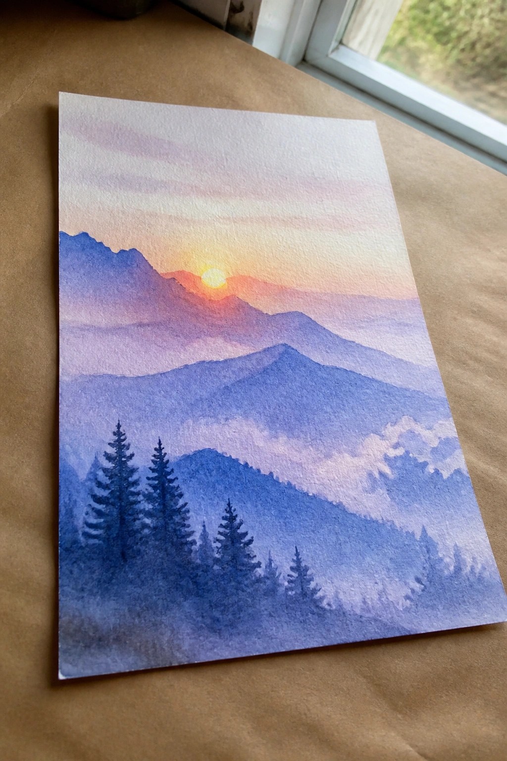 Watercolor painting of layered purple mountains at sunset with orange sun and silhouetted pines