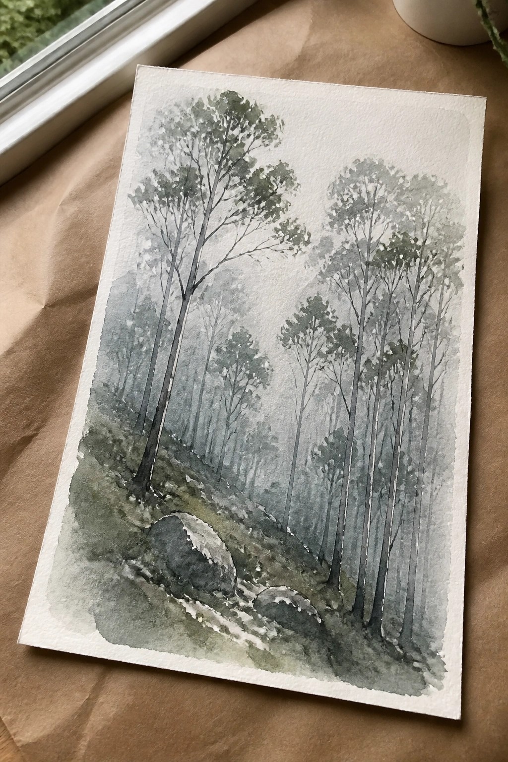 Watercolor forest scene with tall misty trees, rocks, and soft green-gray tones.