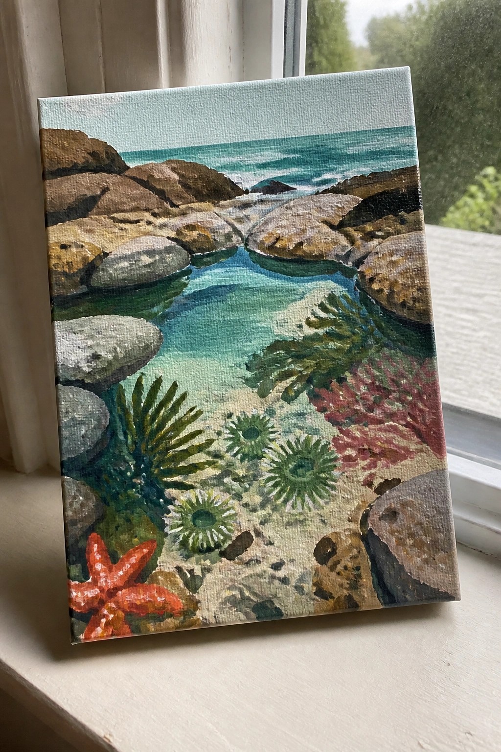 Painting of rocky tide pool with orange starfish, green seaweed, and turquoise water