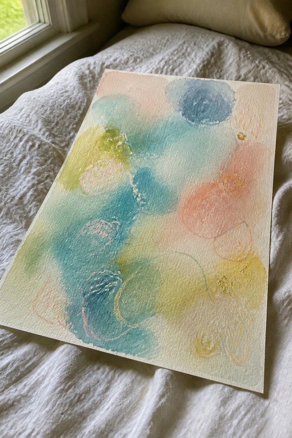 Abstract watercolor painting with blue green pink circles and gold on white bedding