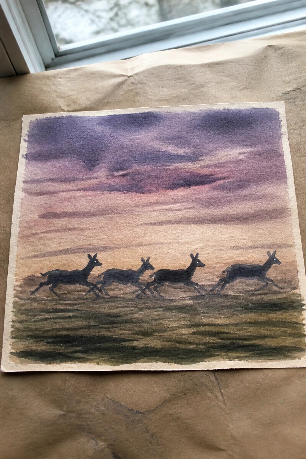 Four black deer running across a purple-pink sunset in watercolor landscape