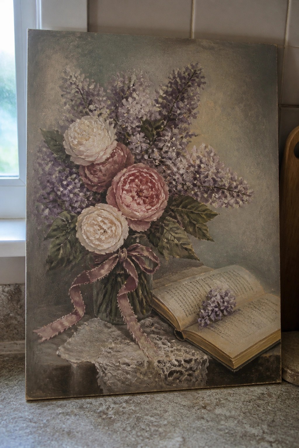 Still life painting of pink peonies, lilacs in ribboned vase beside open book.