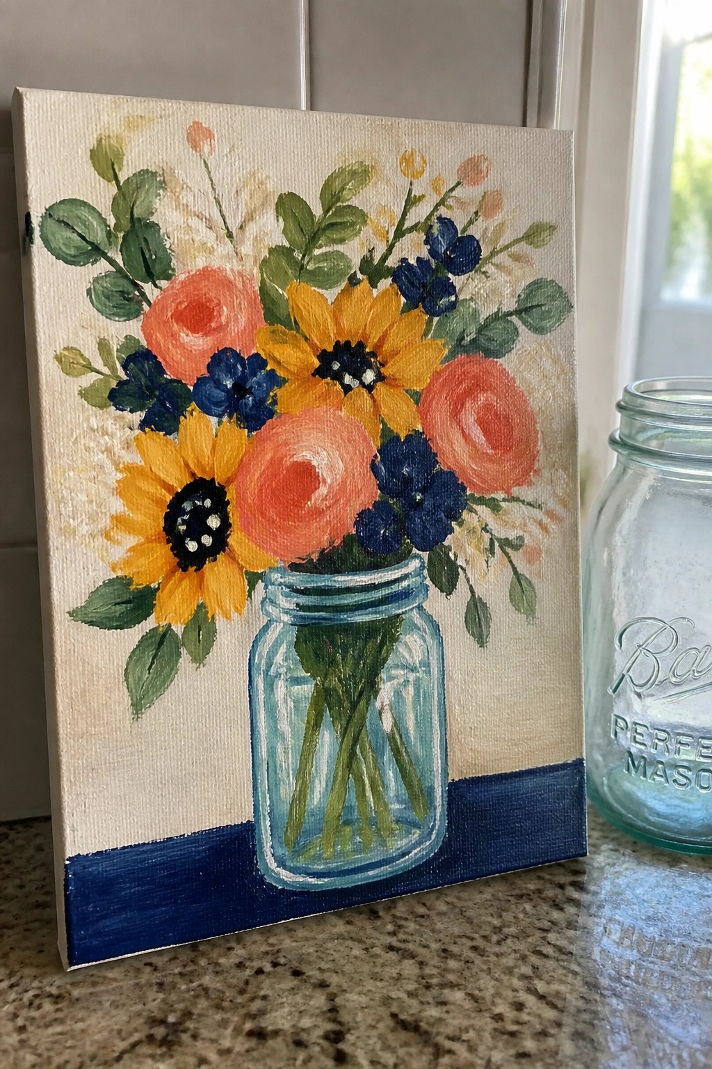 Colorful floral painting in blue mason jar beside empty jar on counter