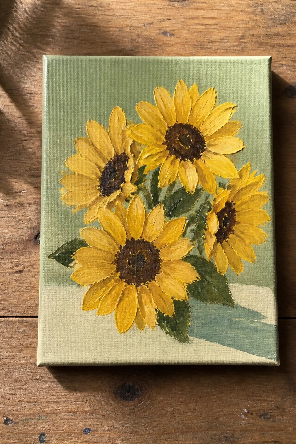 Four yellow sunflowers with brown centers on light green canvas atop wood.