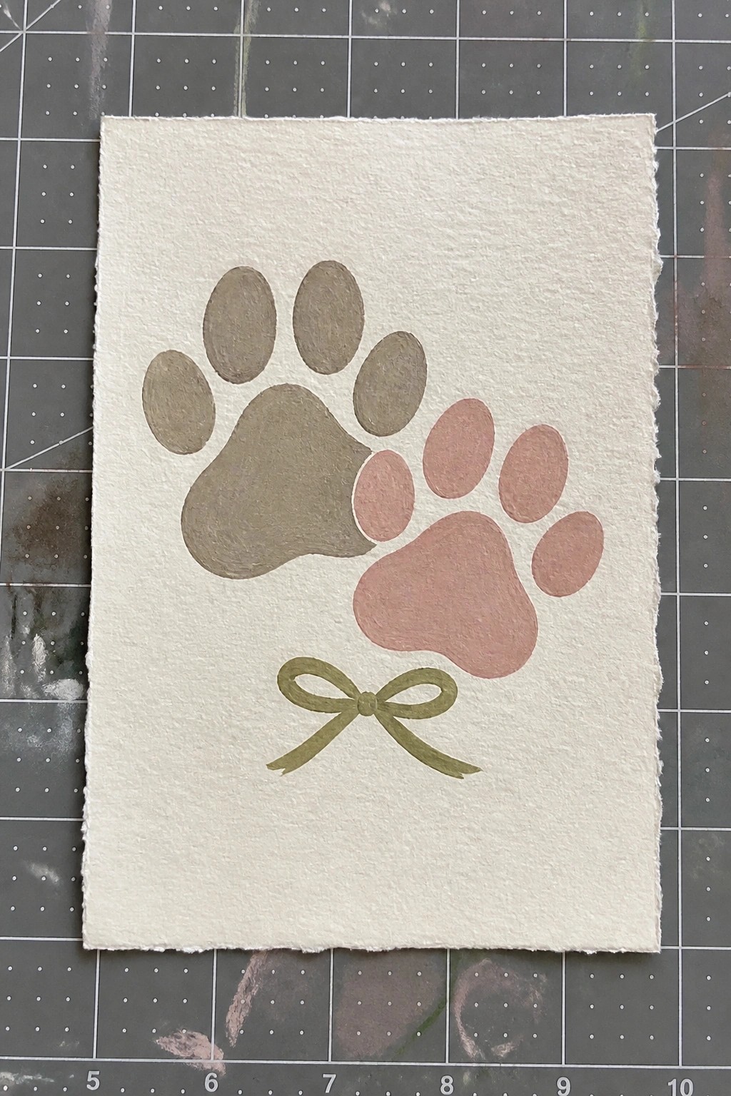 Greenish-brown and pink paw prints with green bow on white paper