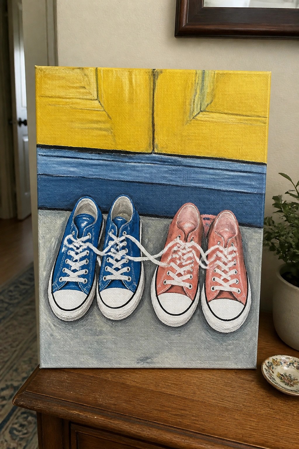 Painting of blue and pink sneakers with laces tied on yellow-blue-gray canvas